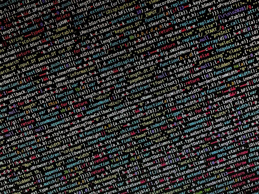 A close-up photograph of a laptop computer displaying lines of code on its dark screen, positioned on a wooden desk surface. To the right of the laptop, partially visible, is a ceramic coffee mug with